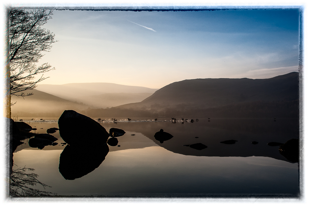 A photograph showing peaceful calm water in the early morning on Ullswater/